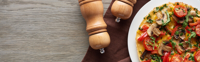 top view of homemade omelet with vegetables on wooden table with pepper and salt