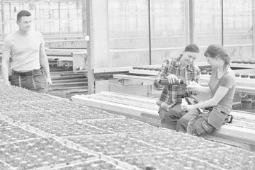 Smiling male botanist looking at female coworkers enjoying coffee break in greenhouse