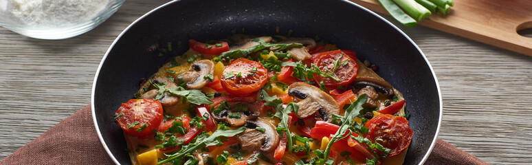 homemade omelet with vegetables and greens in frying pan on wooden table with ingredients