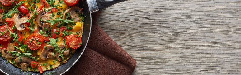 top view of homemade omelet in frying pan on wooden table with napkin