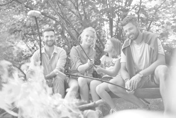 Happy family with male friend roasting sausages over campfire at park