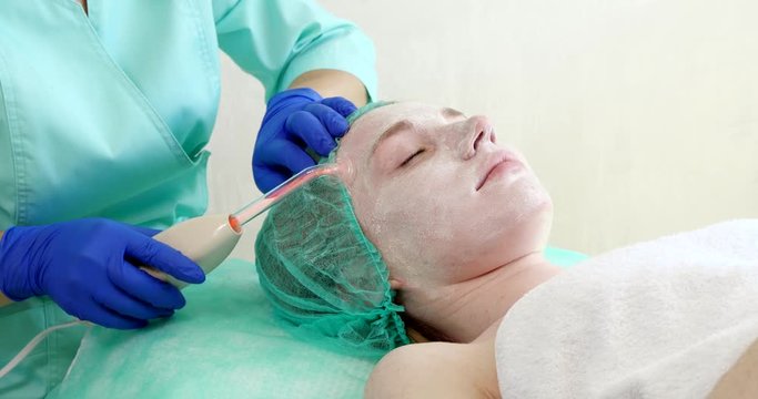 Woman getting electric darsonval facial therapy in salon