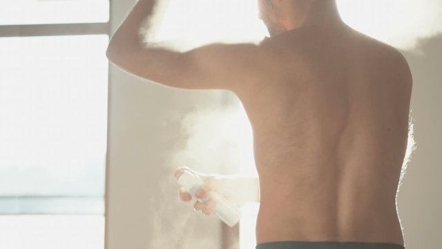 Slow motion well lit video with man after shower spraying deodorant in his armpit abundantly
