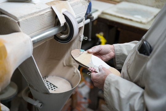 Professional craftsman of orthopedic insoles polishing, sanding and checking in his workshop the modeling of the templates with a fine sandpaper lathe. Hands covered in dust.