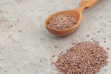 lentils in a wooden spoon, close-up on a gray background. horizontal orientation