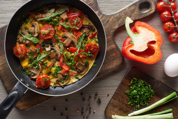 top view of yummy homemade omelet in frying pan with ingredients on wooden boards