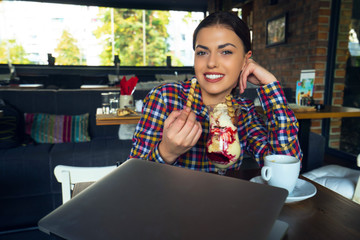 Attractive happy young woman sitting and eating dessert in cafe