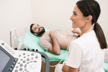 Image of happy man getting abdominal ultrasound scan by female doctor - obrazy, fototapety, plakaty