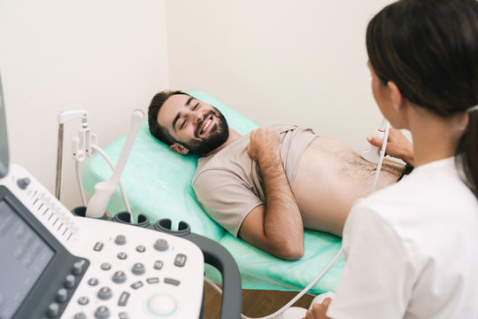 Image of smiling man getting abdominal ultrasound scan by female doctor