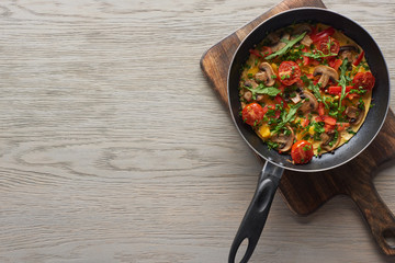 top view of homemade omelet in frying pan on wooden board
