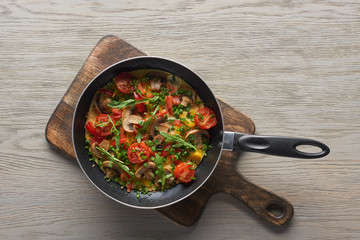 top view of homemade omelet with vegetables in frying pan on wooden board