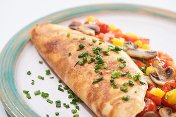 close up of homemade wrapped omelet with mushrooms, tomatoes, greens and peppers on plate
