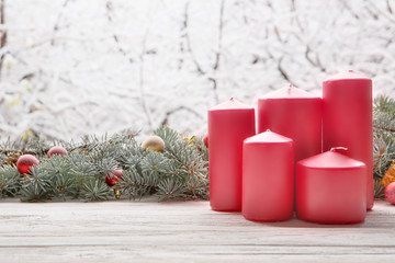 Vintage lantern red candles with Christmas fir tree garland on wooden board on window sill over nature snowing tree park background with copy space