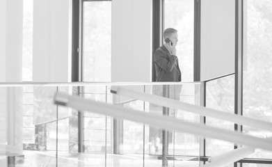 Black and white photo of Young businessman talking on smartphone while standing by railing at office