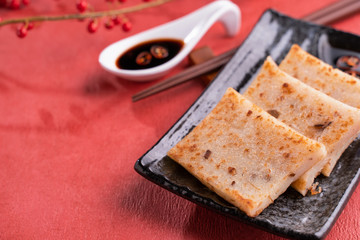 Chinese lunar new year food concept, Delicious turnip radish cake, local cuisine in restaurant with soy sauce on red background, close up, copy space