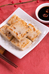 Chinese lunar new year food concept, Delicious turnip radish cake, local cuisine in restaurant with soy sauce on red background, close up, copy space