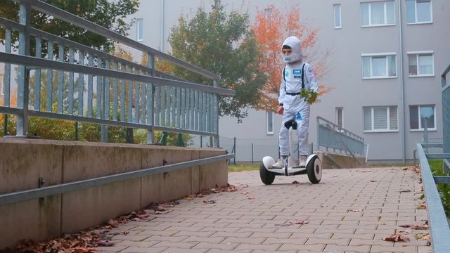 Boy in a suit of an astronaut rides a gyroscooter in the courtyard of the house