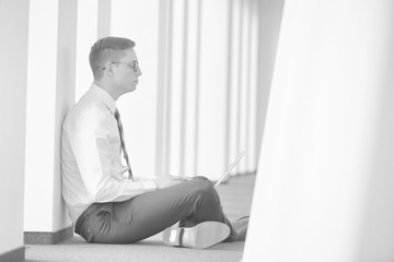 Black and white photo of Young businessman using laptop while sitting on floor at office
