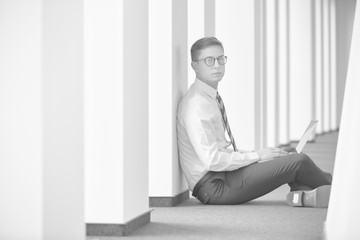 Black and white photo of Young businessman using laptop while sitting on floor at office