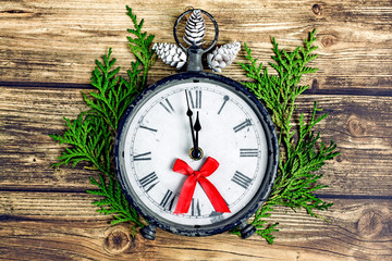 New Year's clock at midnight. New Year's clock shows midnight. Antique clock with roman numerals on a wooden table near fir branches, cones and a red bow. Christmas and new year concept.