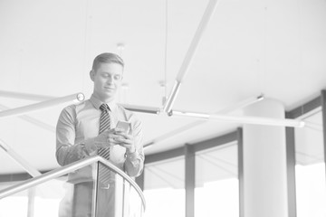 Black and white photo of Smiling businessman using smartphone while standing at office