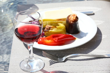 Close-up of a glass of red wine on a blurred background of a white dish with stewed vegetables.Solar table lighting.Lunch on the veranda