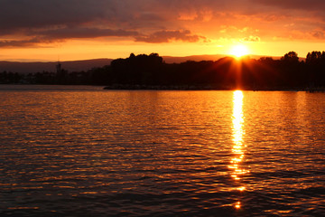 Fototapeta premium A sunset at a lake is coloring the water with yellow and golden colors. Location: Lake Geneva, Lausanne, Switzerland.