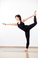 Obraz premium Flexible woman, yogi performing stance in popular Lord of dance pose. Female athlete in black on white background. Concept of attraction to perfection, body and mind unity. Vertical side portrait