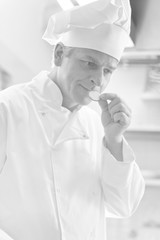 Black and white photo of Mature chef smelling fresh cucumber while standing at restaurant kitchen
