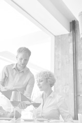 Black and white photo of Young waiter showing menu to mature couple at restaurant