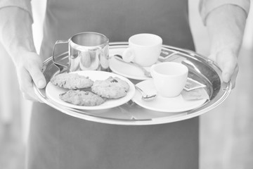 Young waiter serving coffee and cookies at restaurant