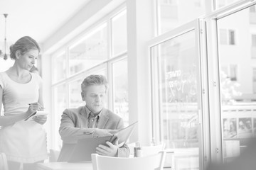 Young waitress taking order from mature customer at restaurant