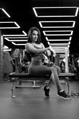 Fototapeta na wymiar Beautiful fitness brunette girl is sitting with dumbbell and posing BW