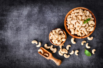 Cashew nuts in wooden bowl on dark stone table with mint leaf on top.