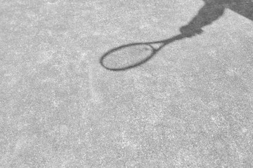 Shadow of mature man hitting tennis ball with racket on red court