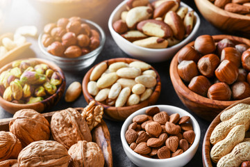 Mixed nuts in wooden bowls on black stone table. Almonds, pistachio, walnuts, cashew, hazelnut. Top view nut photo. - obrazy, fototapety, plakaty