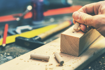 joiner putting dowel pin into a piece of wood - obrazy, fototapety, plakaty