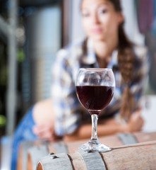girl looking at glass of red wine standing on wooden barrel in winery