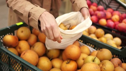 Woman buys fruits in a supermarket, yellow beautiful apples. She puts the bags in reusable bags. Eco packaging, zero waste, stop plastic, vegetarian and raw food diet