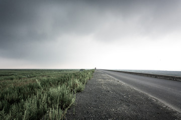 A straight asphalt road under the dark clouds