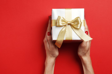 Festive gift box in a female hand on a red background. Place for text.