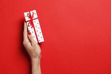 Christmas gift box in a female hand on a red background. Place for text. Top view.