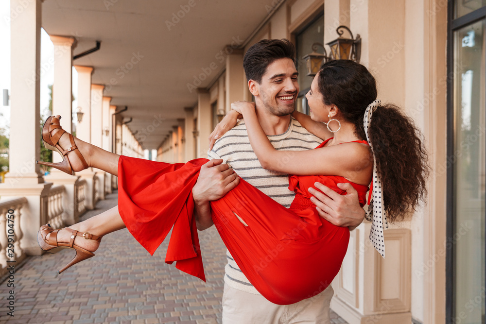 Wall mural image of happy romantic man carrying woman in hands and smiling - Wall murals