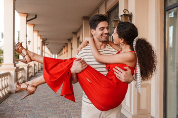 Image of happy romantic man carrying woman in hands and smiling