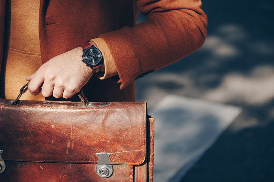 street style 2019 autumn fall fashion, close up detail of men's fashion accessory. man wearing an elegant wristwatch and holding a vintage leather briefcase.