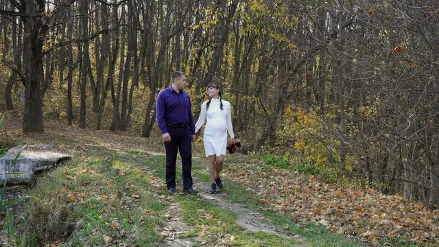 A pregnant couple, a young girl and a guy, walk through the autumn Park holding hands and kissing against the background of a beautiful landscape on a Sunny day. Family walk in nature. Concept. 4K