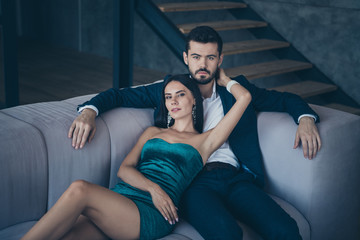 Photo of two classy people couple wealthy guy and lady lying close on comfy couch tenderness evening party look wear formalwear suit short mini shiny mini dress indoors
