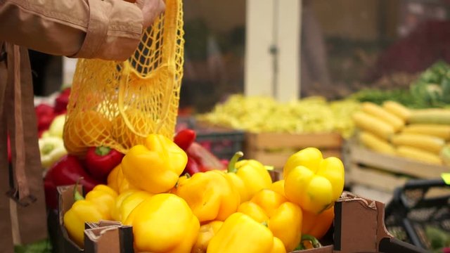 Close-up female hands stack yellow pepper in a string bag. Eco packaging, zero waste, vegetarian food