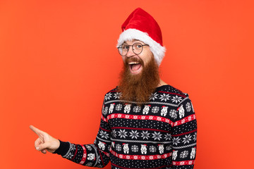 Christmas man with long beard over isolated red background surprised and pointing finger to the side