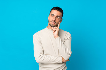 Young man over isolated blue background thinking an idea while looking up